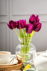 Green tea in a white porcelain cups and teapot, tulips in a glass vase, mimosa flowers, light background. Tea party.