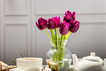 Green tea in a white porcelain cups and teapot, tulips in a glass vase, mimosa flowers, light background. Tea party.