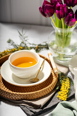 Green tea in a white porcelain cups and teapot, tulips in a glass vase, mimosa flowers, light background. Tea party.
