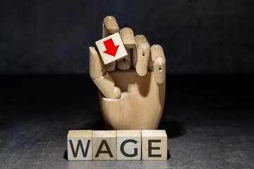 sztuczna ręka trzymająca kostkę z czerwoną strzałką w dół nad napisem na kostkach: WAGE. 