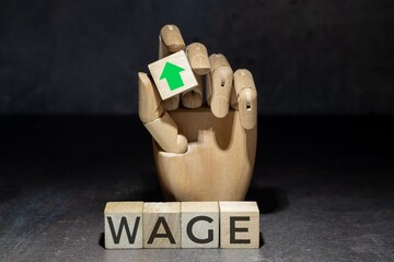 sztuczna ręka trzymająca kostkę z zieloną strzałką w górę nad napisem na kostkach: WAGE. 