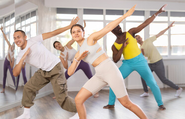Cheerful emotional sporty young female dancer rehearsing popping techniques during group workout in...