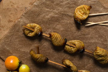 Overhead view of roasted sago worms, top view of palm worms, roasted grub worms on a brown countertop