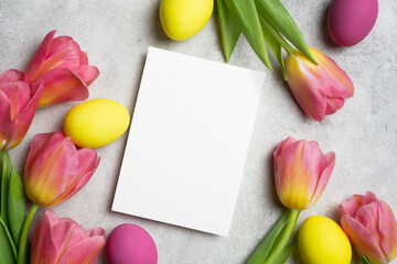 Happy Easter greeting card mockup, blank paper card mock up with colored easter eggs and fresh tulips flowers decoration, top view with copy space