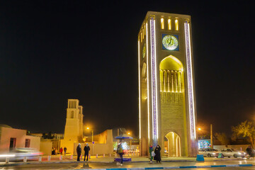 Nightlife on the streets of Yazd, Iran. The clock tower of Saat Square is visible in the center. Figures of passersby, cars and police officers are visible, blurred in motion