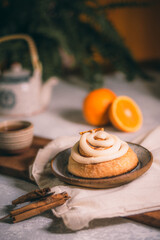 A cozy cinnamon roll with glaze on a rustic plate, surrounded by spices and oranges. Warm tones and soft lighting create a homemade, inviting bakery scene.
