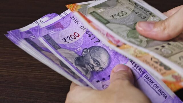 Close up view of woman's hands counting Indian currency notes (INR). Indian cash money of 500, 200 and 100 rupees denominations. Real time motion video.