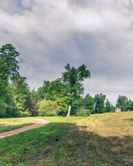 Path winds through a park with trees and a house in the distance