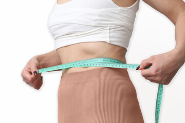Slim woman measuring her waist with a tape. Fitness and weight loss concept showing a toned belly...