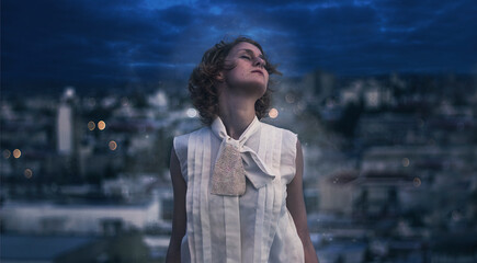 Carefree woman with her head tipped back standing outdoors with a city backdrop at night