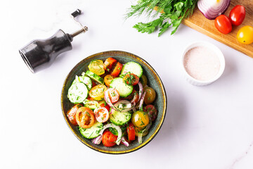 Fresh juicy summer salad with cherry tomatoes, cucumbers, aromatic dill, sweet onion and olive oil in dark ceramic bowl top view. Healthy vegan food concept.