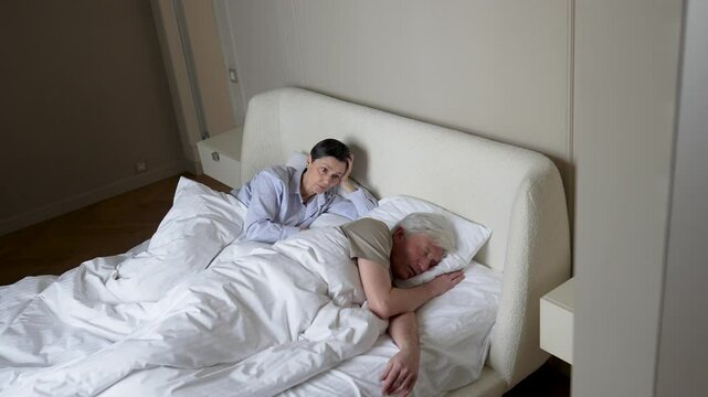 Angry desperate sleepless mature woman pushes snoring husband, frustrated by restless night. Sleep deprivation, breathing issues apnea, inability to rest, hopelessness, disturbed night, irritated wife