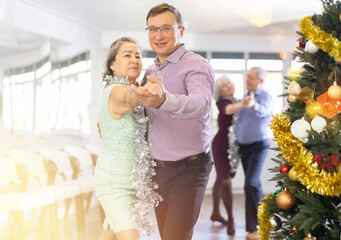 Happy caucasian man and old lady practising paired latin dance in modern dance studio during celebration Christmas and New Year