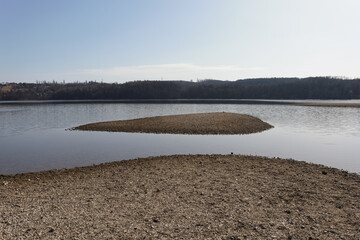 Beach and small island. Minimalist winter landscape of water reservoir and lake. Beach with rocks and pebbles. 