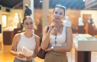 Adult woman and teenage girl with brochure looking at sculptures in museum hall