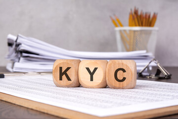 the acronym 'KYC' on wooden cubes placed on an office desk with documents, symbolizing financial...