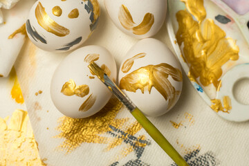 A person decorates an Easter egg with a paintbrush, with colorful eggs in a carton and paints nearby. Ideal for spring celebrations, family fun, or artistic projects.