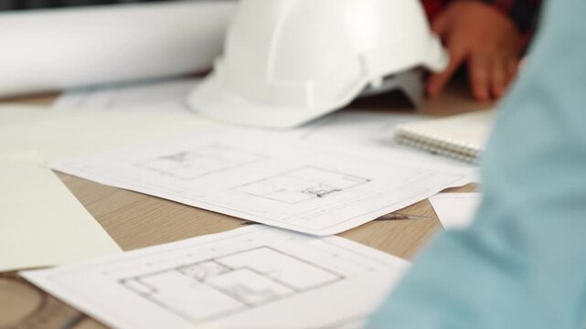 Architect and safety engineer discussion about building blueprint displaying on laptop on table with architectural document and wooden block scatter around at modern office. Closeup. Delineation.