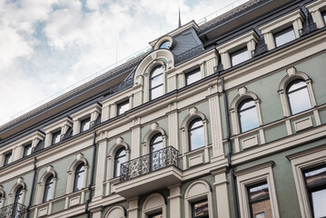 Upper part of a facade of an old green building with beige window surrounds. Looking up at the rooftop of a building in old town.