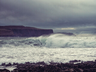 The ocean is rough and the sky is cloudy. The waves are crashing against the rocks. Scene is tense and dramatic. Nobody, Dark and moody nature background.