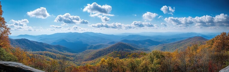 Naklejka premium Breathtaking Panoramic View of Colorful Autumn Foliage Overrolling Mountains Under Bright Blue Sky with Fluffy White Clouds