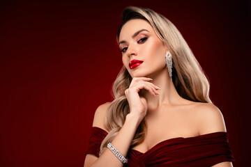 Obraz premium Elegant young woman with glamorous makeup and accessories against burgundy background