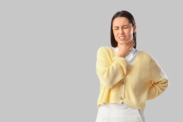 Young woman suffering from sore throat on grey background