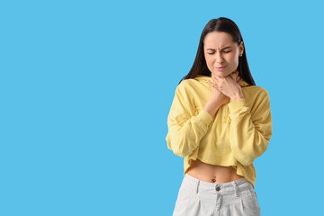 Young woman suffering from sore throat on blue background