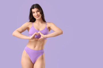 Naklejka premium Pretty young woman in underwear making heart with her hands on lilac background
