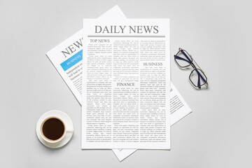 Different newspapers with glasses and cup of coffee on grey background