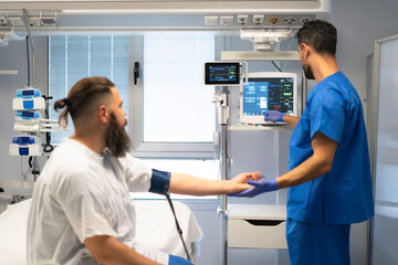 Doctor checking patient's pulse and examining medical data on monitor in hospital room