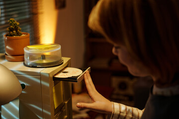 Person's hand retrieving a CD-ROM from an external drive in a cozy home office environment. Cactus plant and ambient lighting in the background creating a warm atmosphere