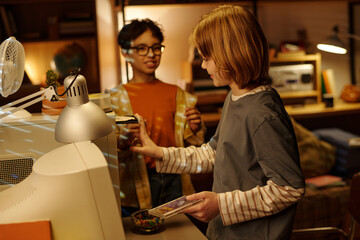 Two children in cozy living room interacting with modern technology and working on creative projects together, surrounded by a warm, inviting atmosphere