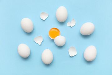 Whole and cracked chicken eggs on blue background