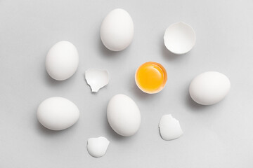 Whole and cracked chicken eggs on grey background
