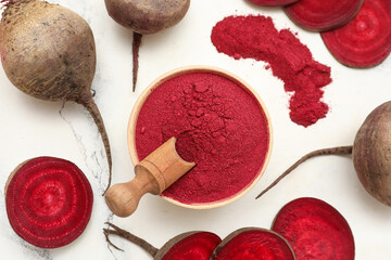 Wooden bowl of vibrant beetroot powder with scoop, fresh beets and slices on light background