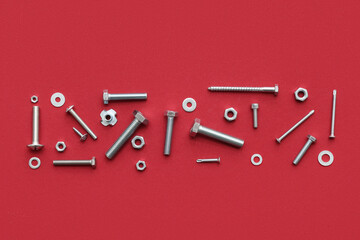 Different tap bolts, screws and chrome nuts on red background