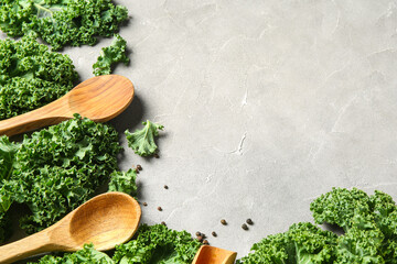 Fresh leaves of kale cabbage with wooden spoons and peppercorns on grey background