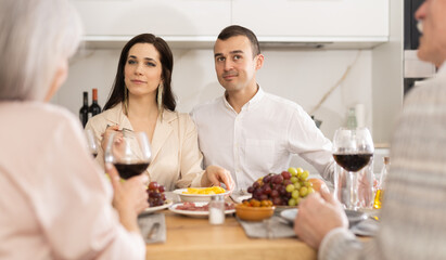 Happy young couple talking with senior parents while having wine sitting around kitchen table