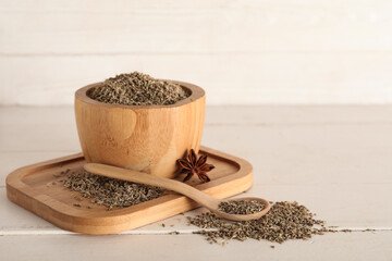 Board with bowl of dried seeds, anise and spoon on white wooden background