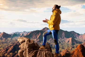 Fototapeta premium Alone traveler stands on a mountain summit soaking in the stunning view of peaks, clouds and endless sky, adventure seeker. Breathtaking scenery symbolizes determination and ambition.