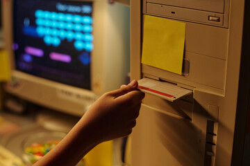 Close-up view showing hand pushing floppy disk into drive of a computer system. Background displays...