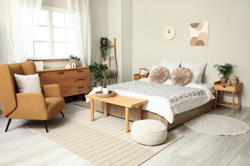 Obraz premium Interior of light bedroom with bedside tables, armchair, chest of drawers and big bed