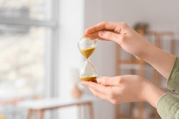 Woman holding hourglass at home, closeup