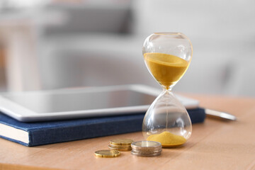 Hourglass with coins on table in room, closeup