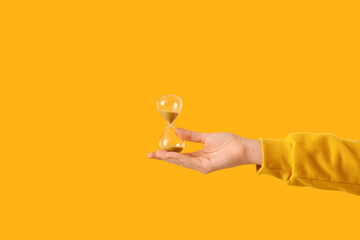 Woman holding hourglass on yellow background