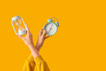 Woman holding hourglass with alarm clock on yellow background
