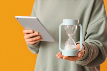 Woman with hourglass and tablet computer on yellow background, closeup