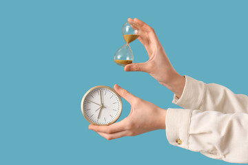 Woman holding hourglass with alarm clock on blue background
