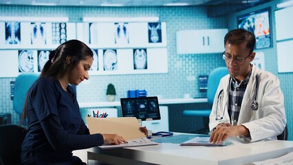 Fototapeta premium Indian healthcare expert sharing medical expertise with a patient in clinic, reviewing x ray scans and MRI diagnostics to focus on accurate treatment and recovery. Insurance check up. Camera B.